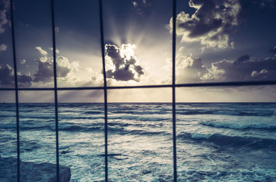 Scenic view of sea seen through railing against cloudy sky during sunset
