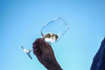 Cropped image of person holding wineglass against clear blue sky