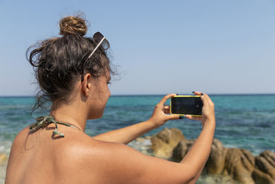 Portrait of teenager girl touching a modern mobile against the beach