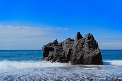 Rock formation on sea shore against blue sky