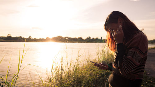 Woman standing by lake against sky during sunset