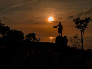 Silhouette person standing by tree against sky during sunset