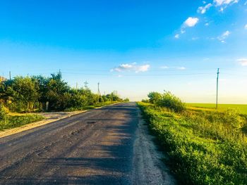 Road amidst trees on field against blue sky