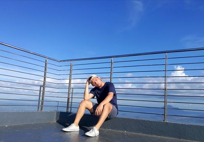 Man sitting on railing against blue sky