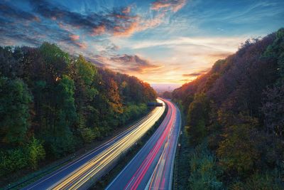 Light trails on road amidst trees against sky during sunset