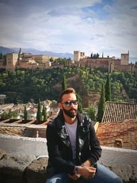 Portrait of young man sitting on sunglasses against cityscape