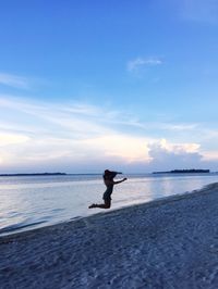 Silhouette woman jumping at beach against sky during sunset