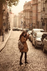 Side view of young woman with backpack standing on street in city