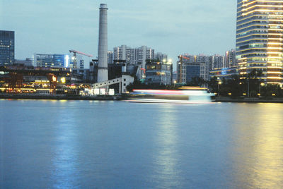 Illuminated buildings by sea against sky in city