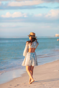 Rear view of woman standing at beach against sky during sunset