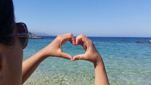 Cropped image of woman making heart shape against sea at beach