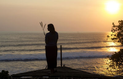 Rear view of silhouette man standing at beach during sunset