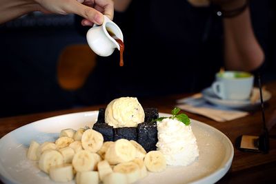 Cropped hand pouring syrup on dessert