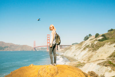 Full length of woman standing on cliff against clear blue sky