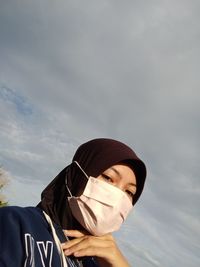 Low angle view of woman wearing mask standing against sky