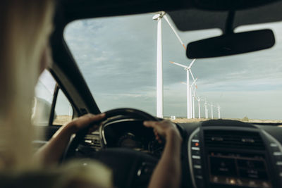 Hands of woman driving car at wind park