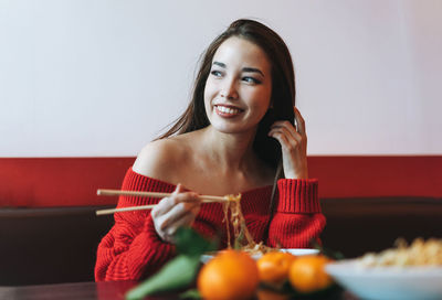 Beautiful smiling young asian woman in red clothes eating asian food in chinese  restaurant