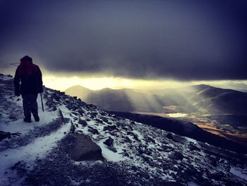 Rear view of person hiking on mountains against cloudy sky during sunrise