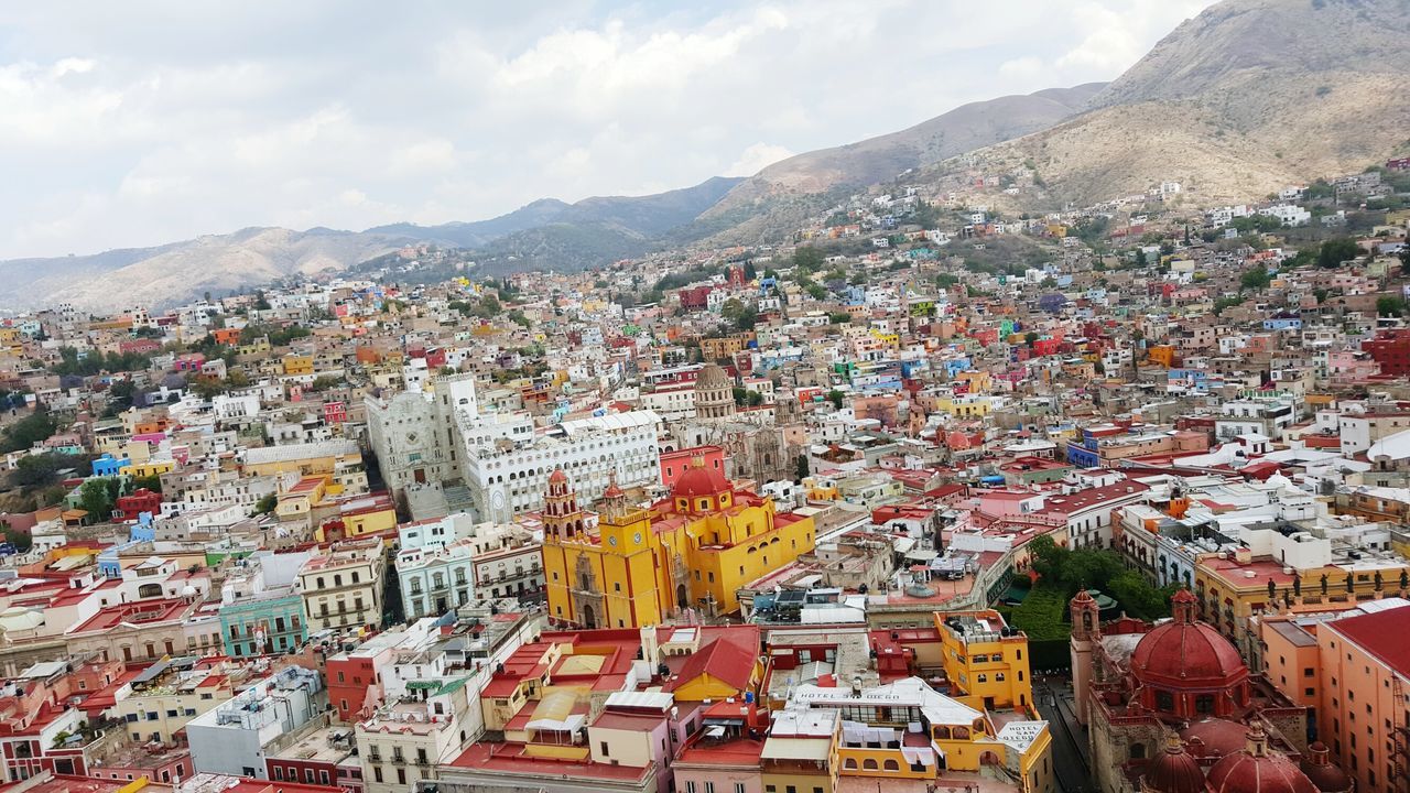 building exterior, architecture, built structure, mountain, residential district, cityscape, crowded, residential building, sky, residential structure, city, house, town, townscape, high angle view, cloud - sky, mountain range, community, outdoors, day