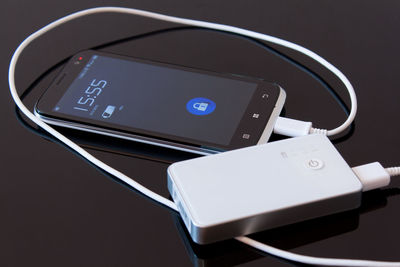 High angle view of smart phone connected to portable charger on black background