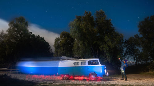 Man standing by car on field against trees at night