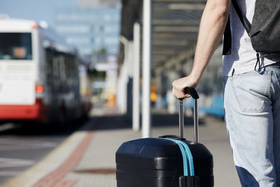 Passenger waiting at bus station in front of airport. selective focus on hand holding suitcace.