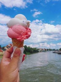 Close-up of hand holding ice cream cone against sky