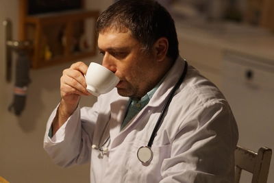 Side view of thoughtful mature doctor drinking coffee sitting in hospital