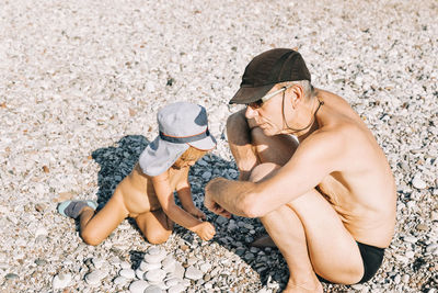 High angle view of shirtless grandfather with naked granddaughter at beach