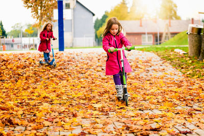 Girls riding push scooters at park during autumn