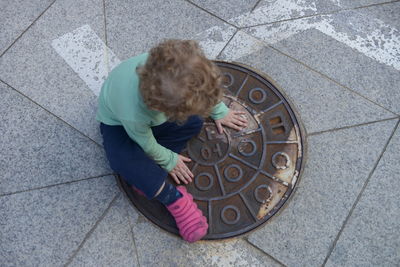 High angle view of boy sitting on sewer at footpath