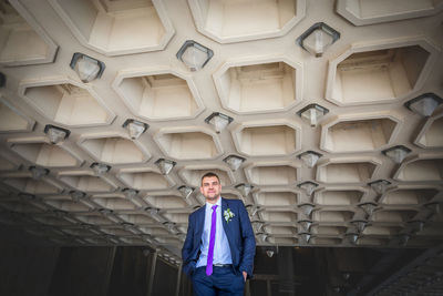 Low angle portrait of handsome bridegroom standing against patterned ceiling