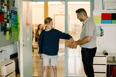 Boy keeping phone while male teacher holding basket in classroom