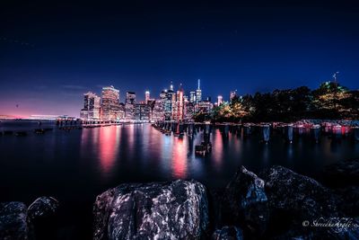 Illuminated buildings by river against sky at night