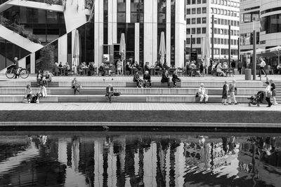 Crowd in city by river against modern buildings