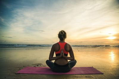 Woman sitting on beach against sky during sunset