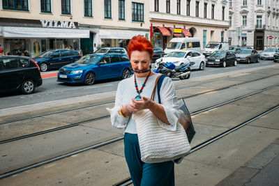 Full length of young woman using mobile phone in city