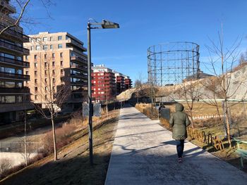 Rear view of woman walking on footpath in city against sky