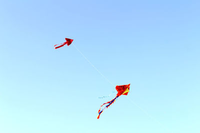 Low angle view of kites flying against clear blue sky