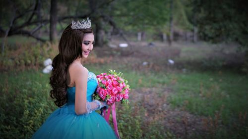 Side view of bride holding bouquet while standing at park