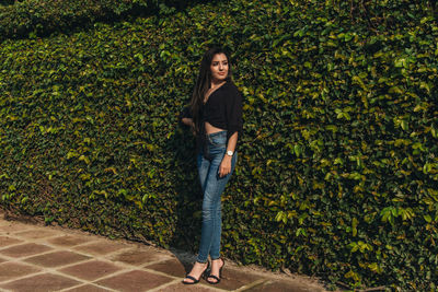 Young woman looking away while standing against plants