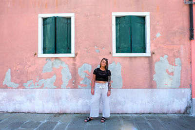 Full length portrait of smiling woman standing against building