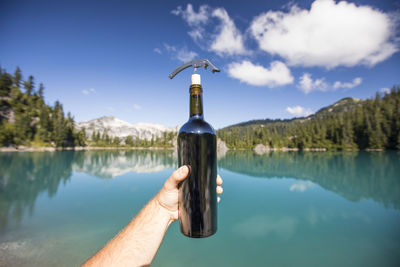 Person holding umbrella by lake against sky