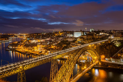 Illuminated bridge over river amidst buildings in city against sky at night