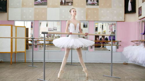 In the ballet hall, girl in white pack is engaged at the ballet, rehearse roleve, goes up on toes
