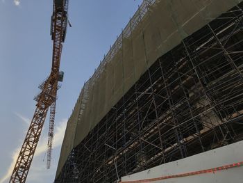 Low angle view of crane at construction site against sky