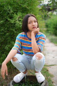 Portrait of teenage girl crouching against plants in park