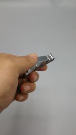Cropped image of man holding nail clipper against wall 