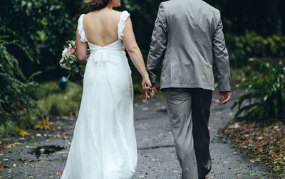 Rear view of newlywed couple holding hands while walking on footpath