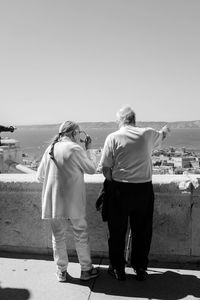 Rear view of couple walking on beach against clear sky